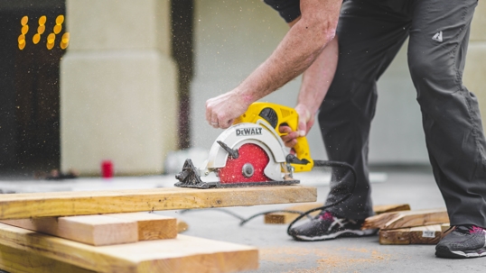 man in black pants using a circular saw to cut wood