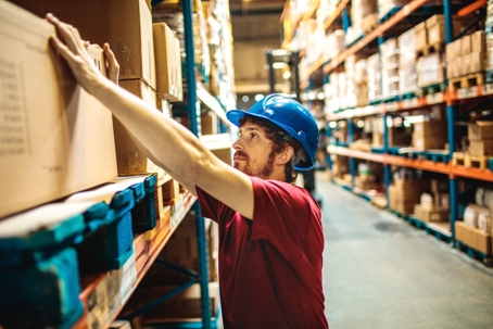 man in hard hat lifting box from shelf in warehouse